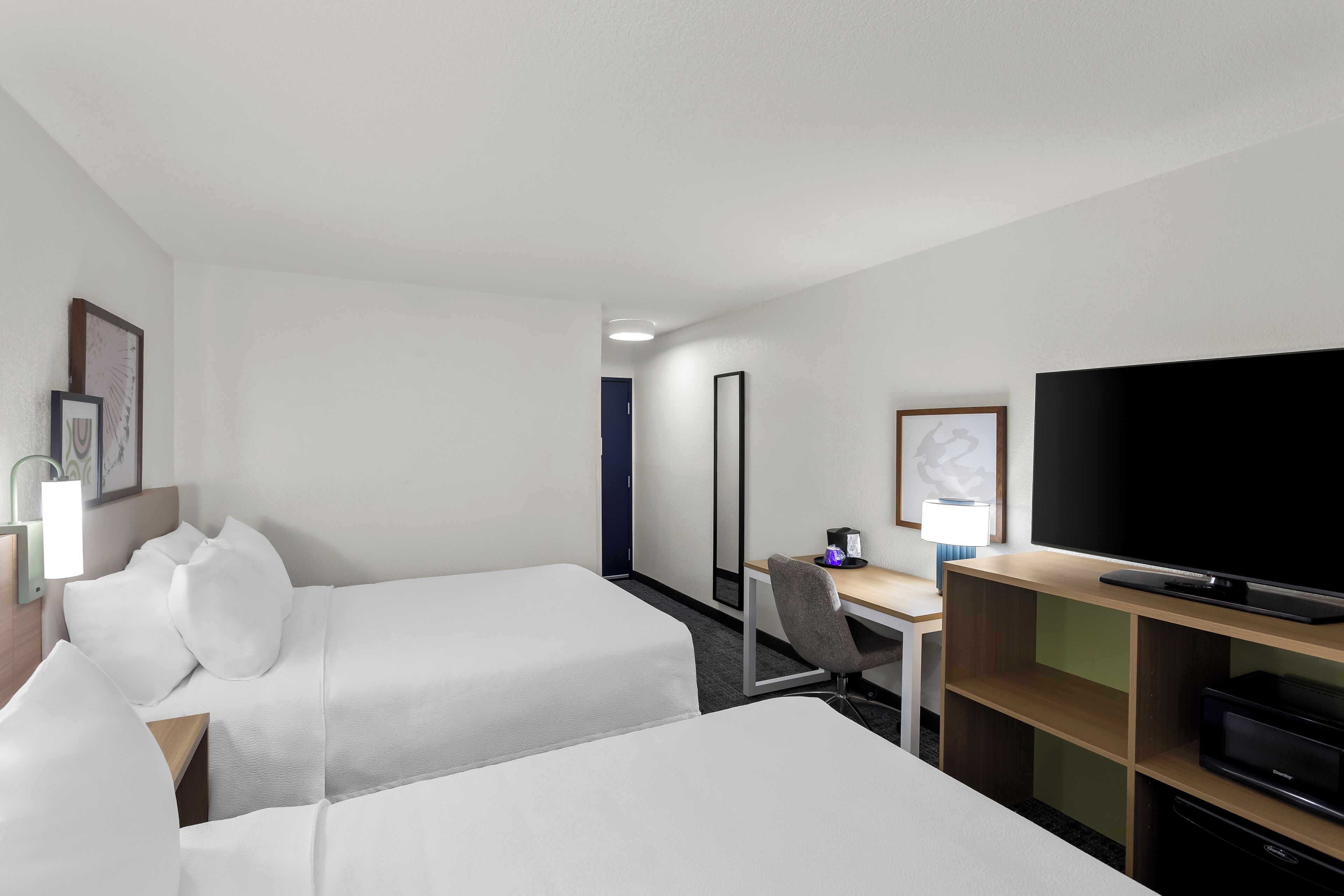 Una habitación de hotel con dos camas, un escritorio, una silla, un televisor y un espejo.