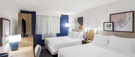 A hotel room with two beds, a desk with a lamp, a chair, a TV, and a window with curtains.