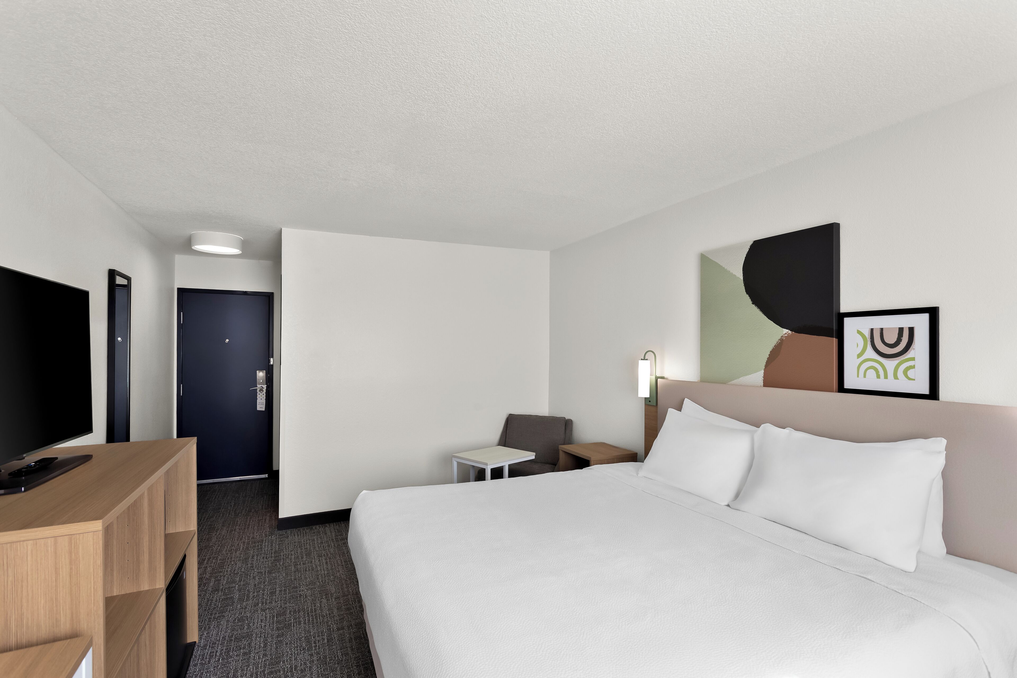 A hotel room with a bed, a desk, a chair, a TV, and a door.