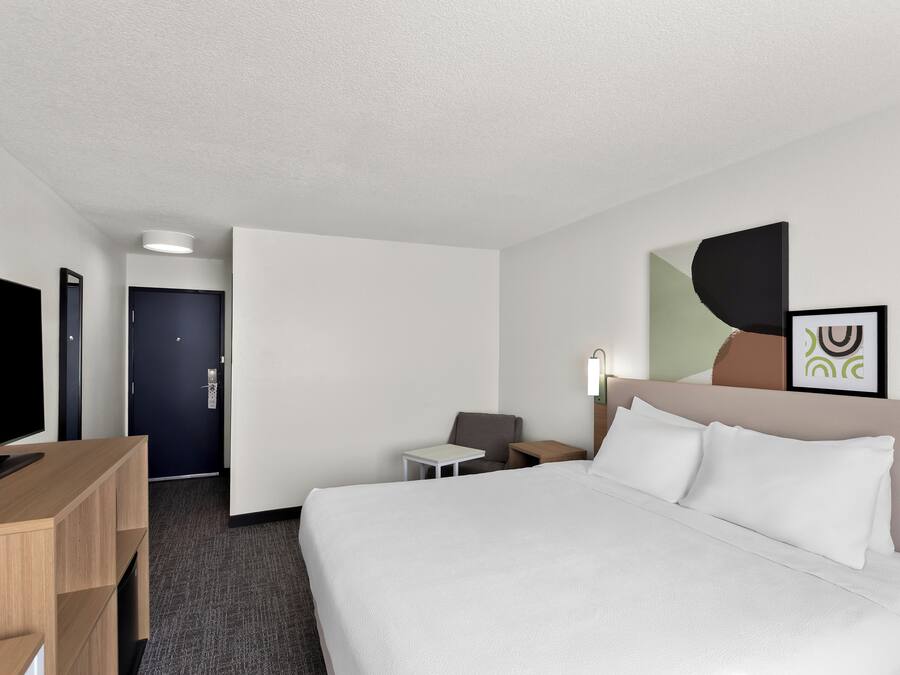 Habitación de hotel con cama, escritorio, silla, televisor y puerta.