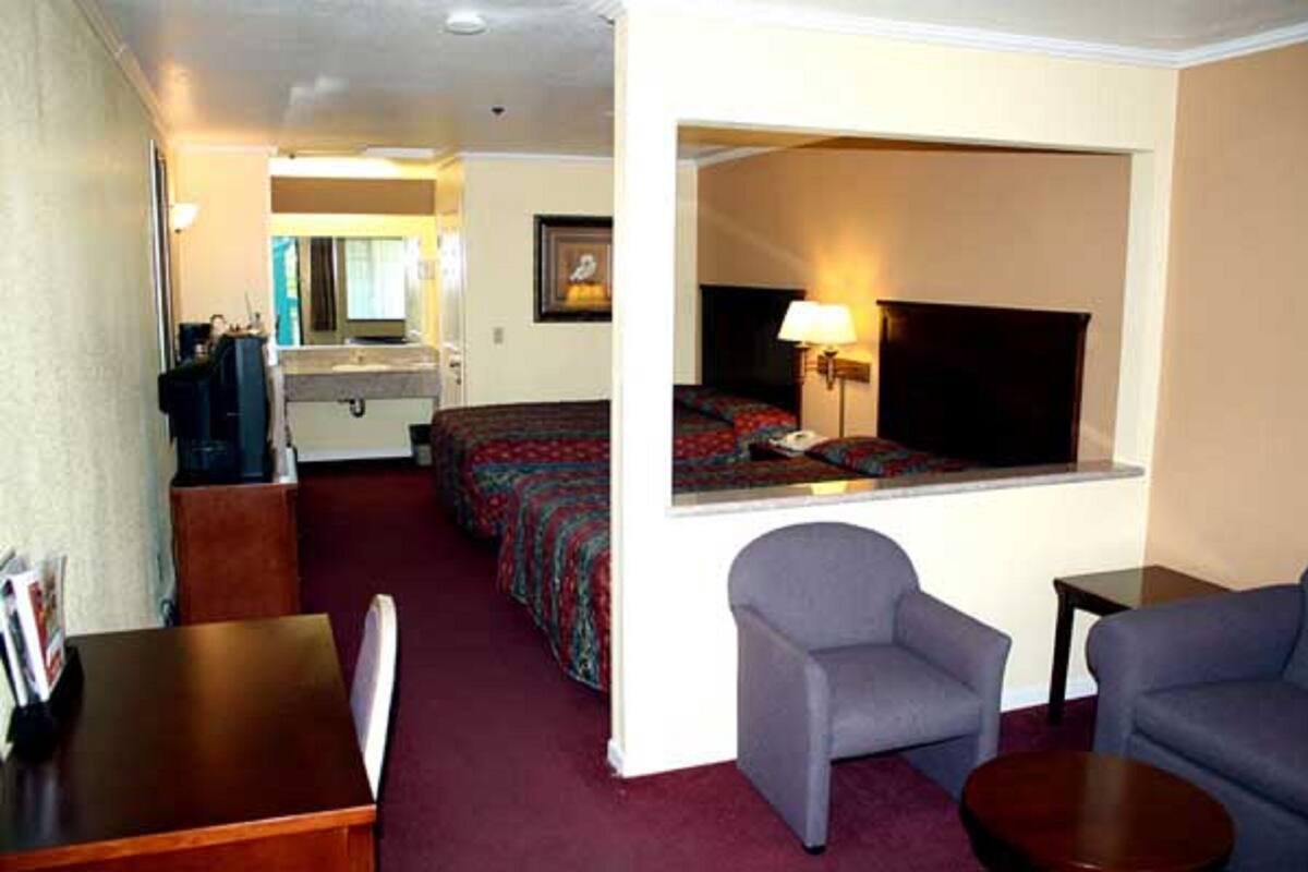 A hotel room with a bed, a desk, a chair, a small table, and a mirror.