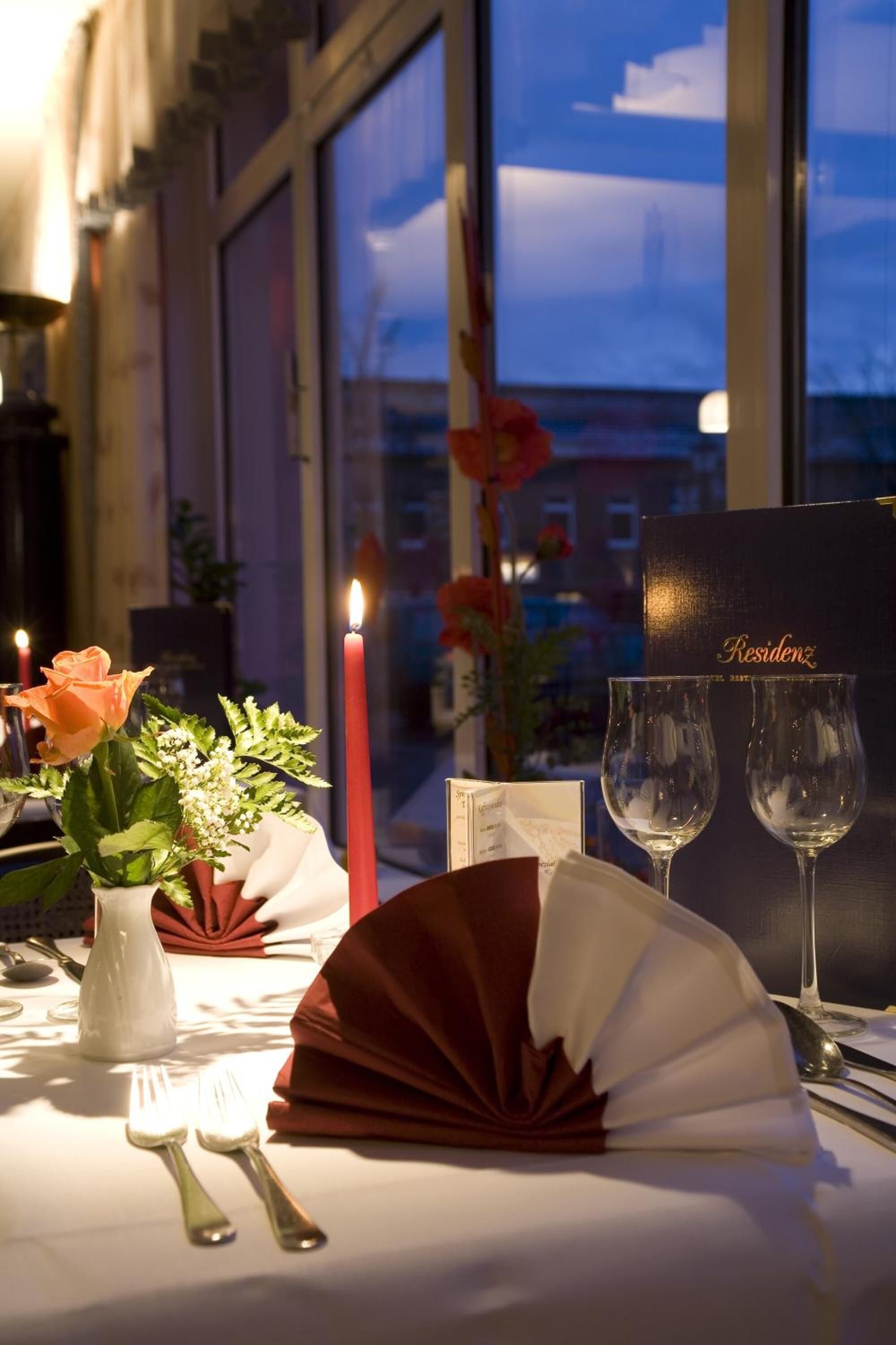 Una mesa para dos, con una vela, un florero con flores y una carta.