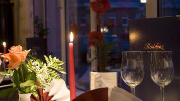Una mesa para dos, con una vela, un florero con flores y una carta.