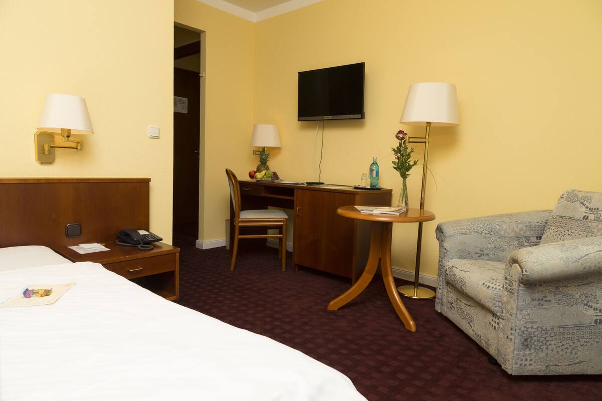 A hotel room with a bed, a desk with a chair, a sofa, and two lamps.