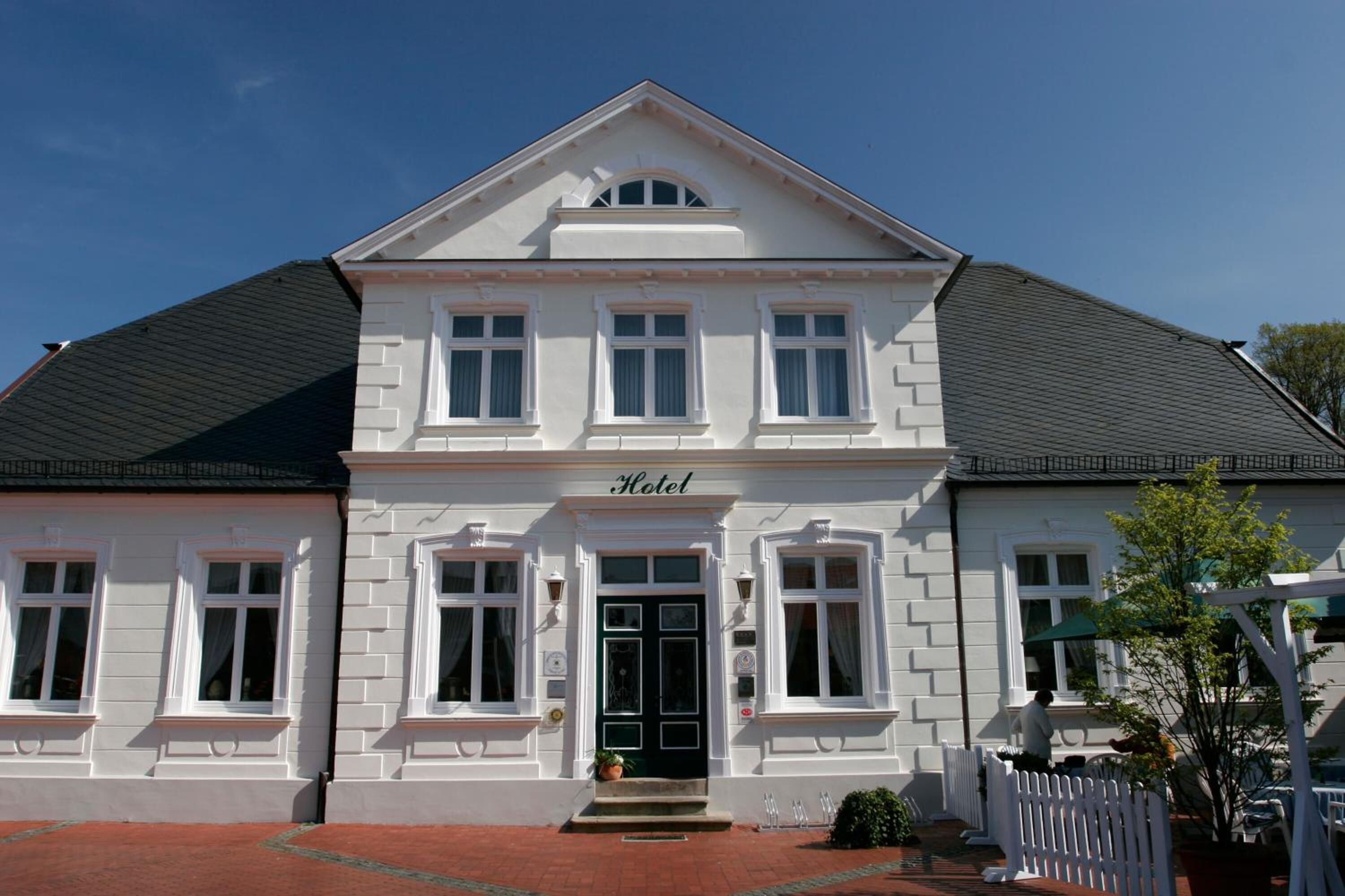 A two-story hotel with a symmetrical facade, a central entrance with a black door, and a sign above the door.