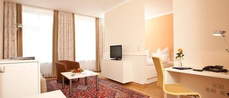 A modern hotel room with a dining area, a TV, a desk with a chair, and a small table with a rug.