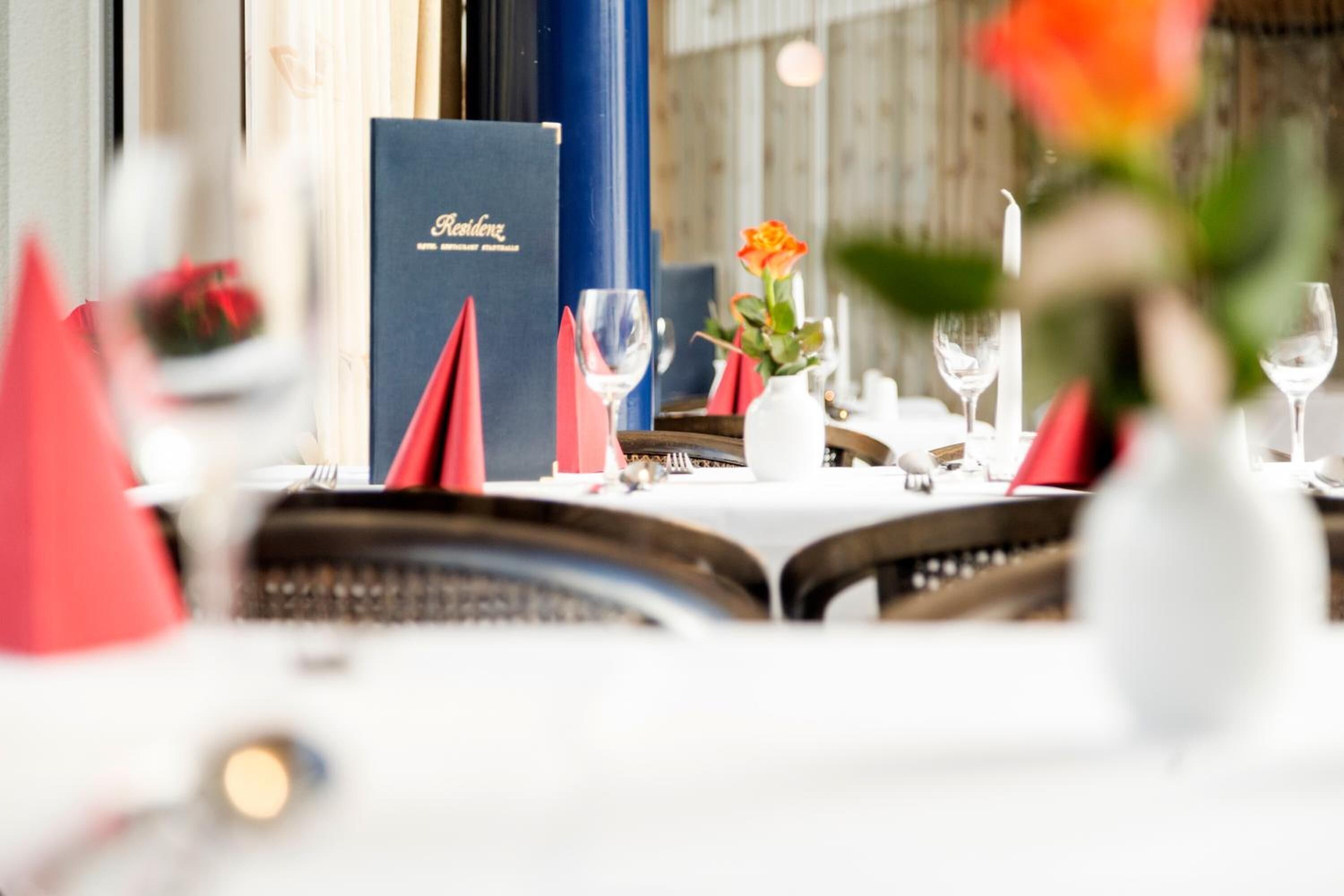 A restaurant setting with a menu stand, a vase with a flower, and a table set for dining.