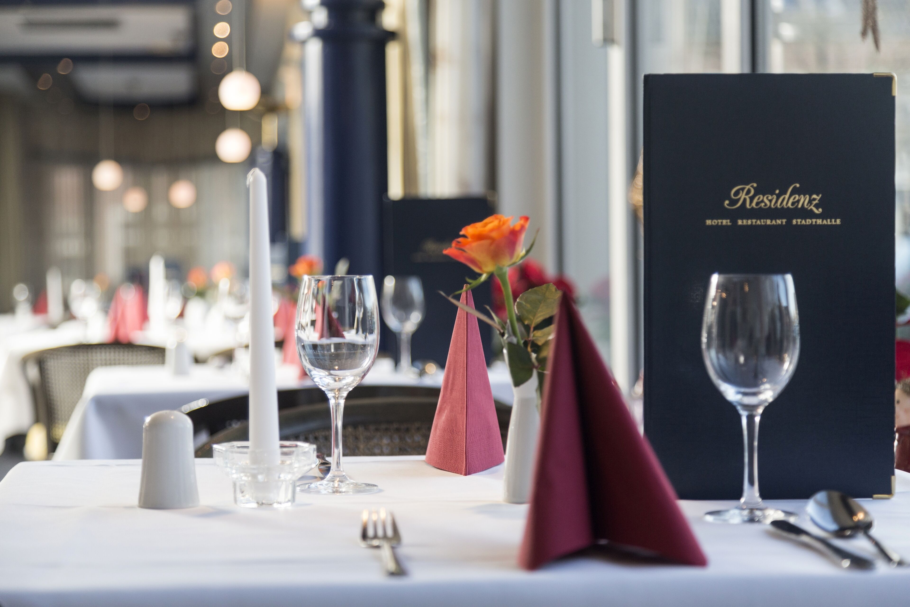 A dining table set with a menu, a rose, a candle, and a glass.