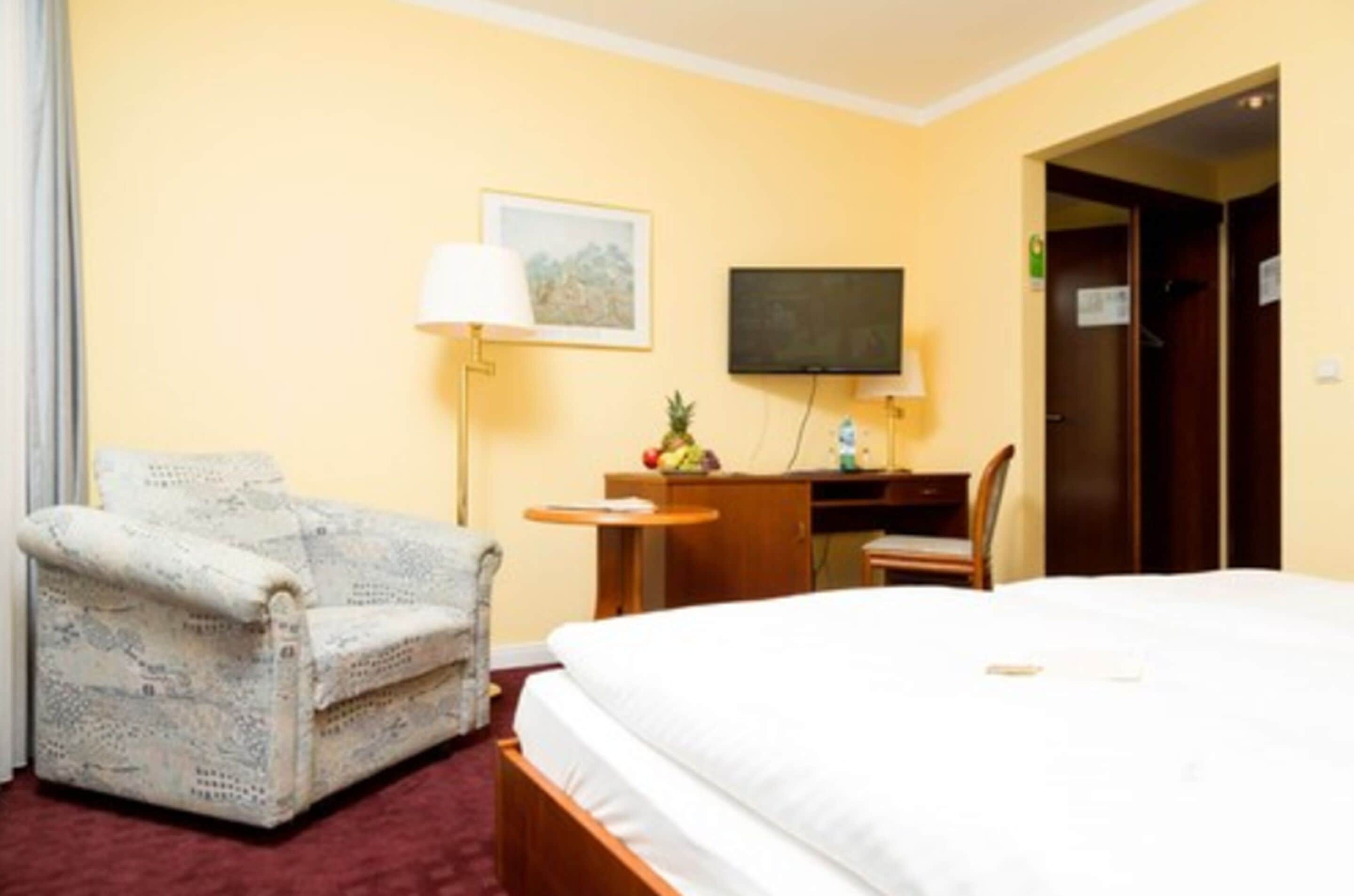 Una habitación de hotel con una cama, un escritorio con una silla, un televisor y una lámpara.