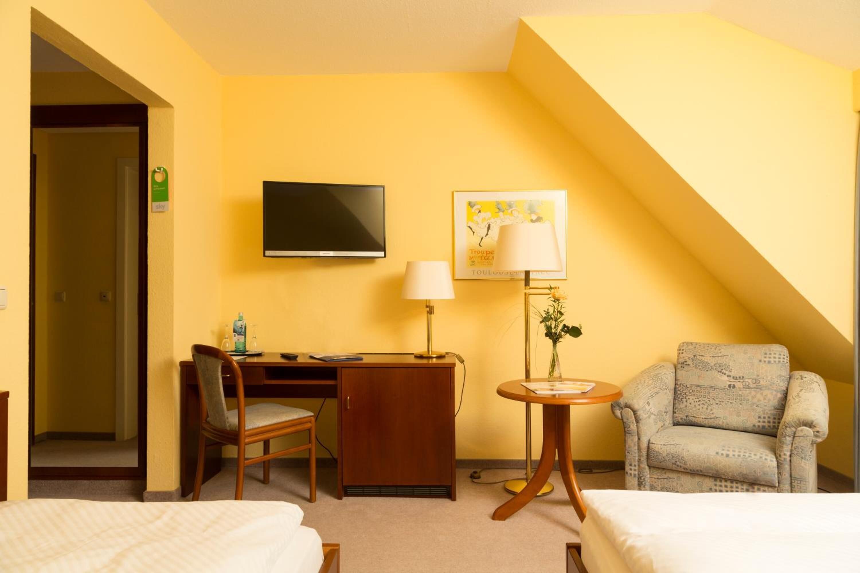 Een hotelkamer met een bureau, stoel, televisie, lamp en twee bedden.
