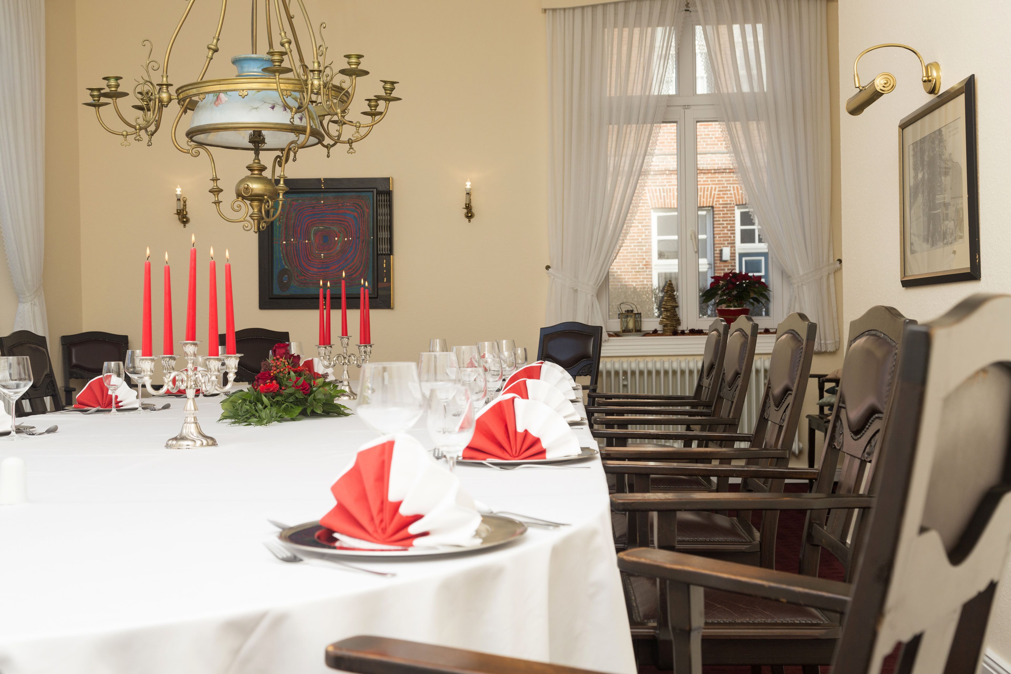 Uma sala de jantar com uma mesa comprida posta para uma refeição, com um candelabro, velas e obras de arte emolduradas.
