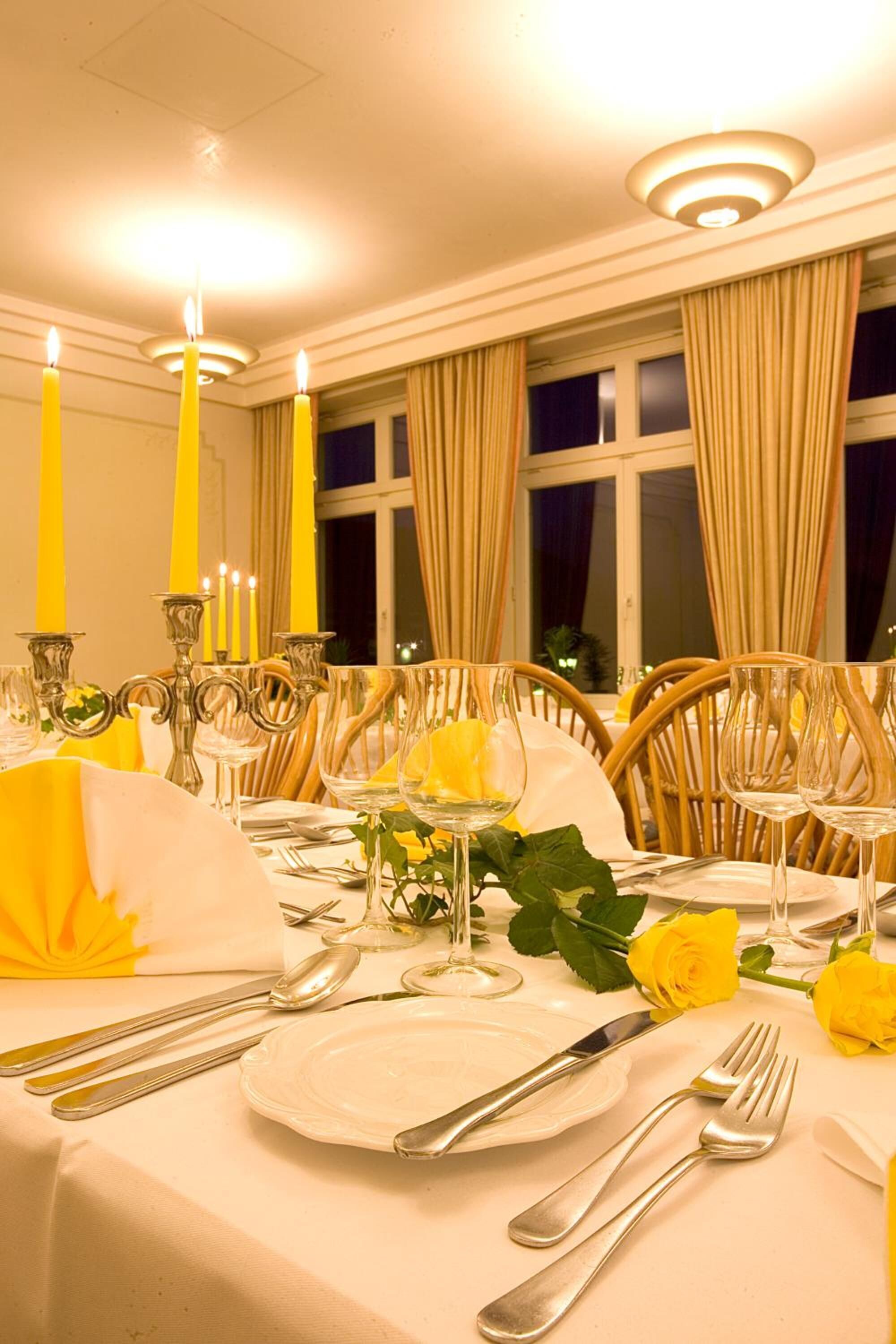Une table à manger décorée avec des bougies jaunes, de la verrerie transparente et une nappe blanche.