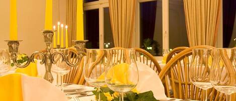 Une table à manger décorée avec des bougies jaunes, de la verrerie transparente et une nappe blanche.