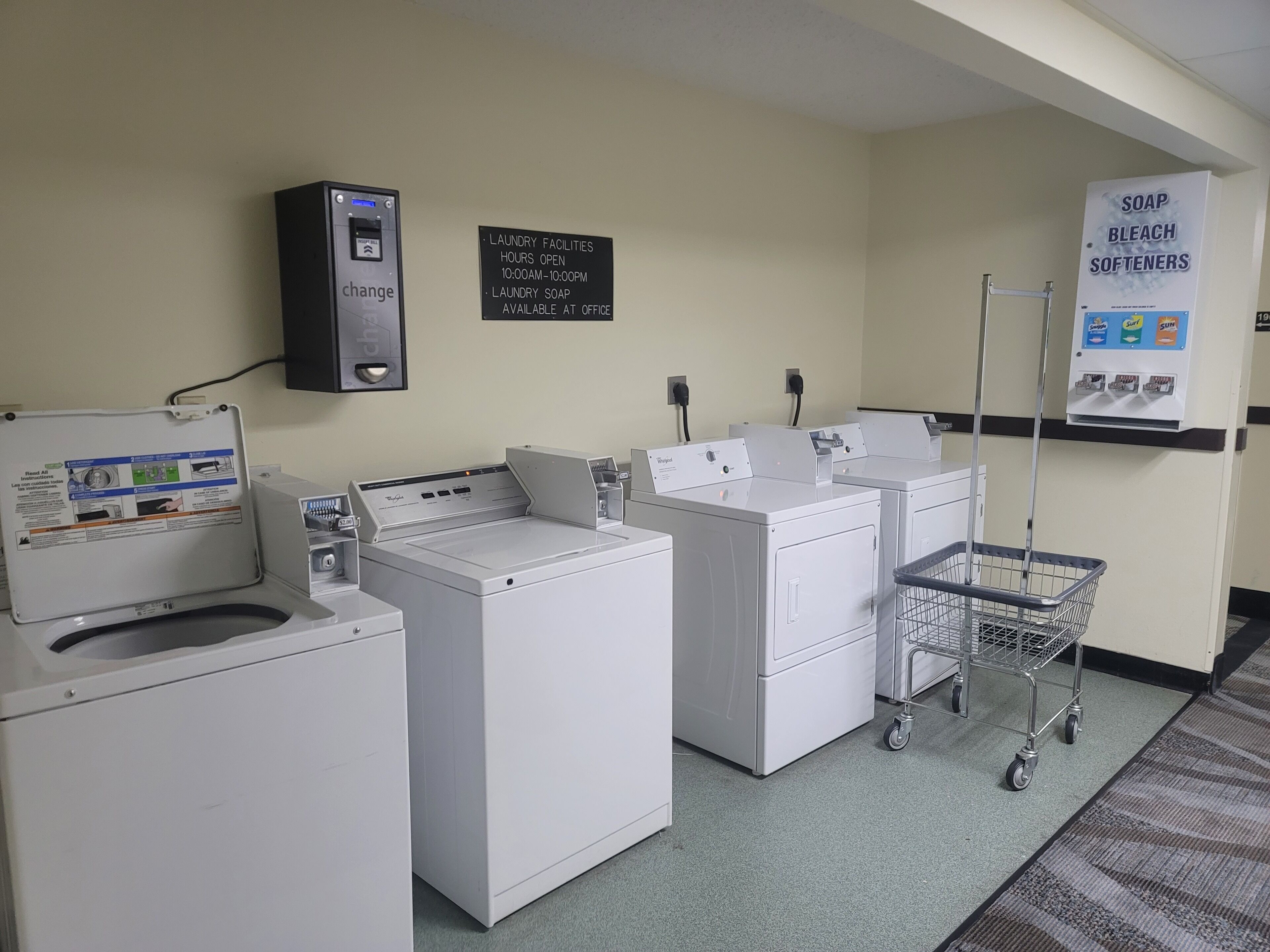 Een wasserette met wasmachines en drogers, een geldautomaat voor muntgeld en een bord met de waszeiten en zeepvoorraad.