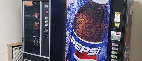 Two vending machines, one with a Pepsi logo and the other with a different design, in a room with tiled flooring and a white ceiling.
