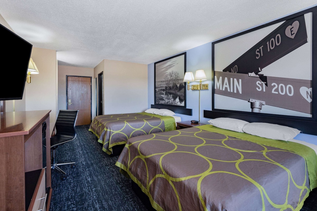 A hotel room with two beds, a desk, and a television.