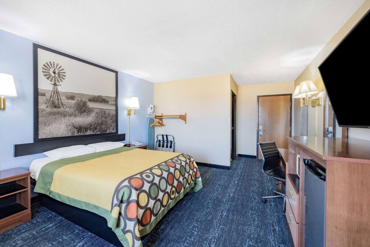 A hotel room with a bed, a desk, a chair, a TV, and a bathroom.