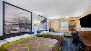 Hotellihuone, jossa on kaksi sänkyä, työpöytä, tuoli, televisio ja suuri ikkuna.