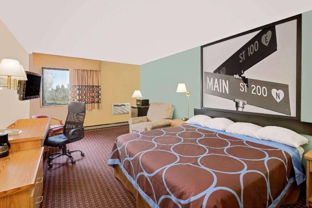 A hotel room with a large bed, a desk, a chair, a television, and a wall-mounted sign.