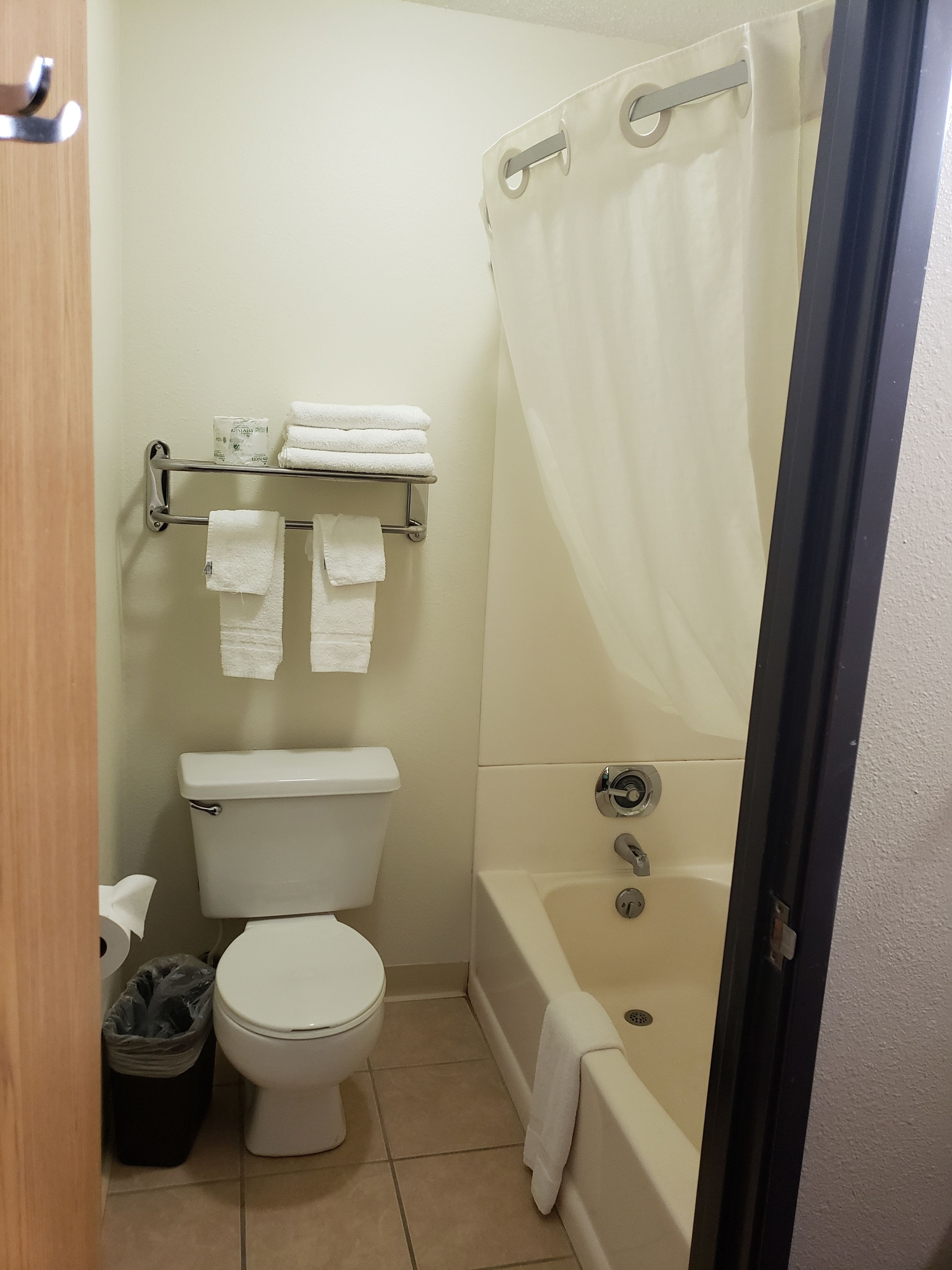 A small bathroom with a toilet, a bathtub, and a shower curtain. There are towels on a rack and a trash can.