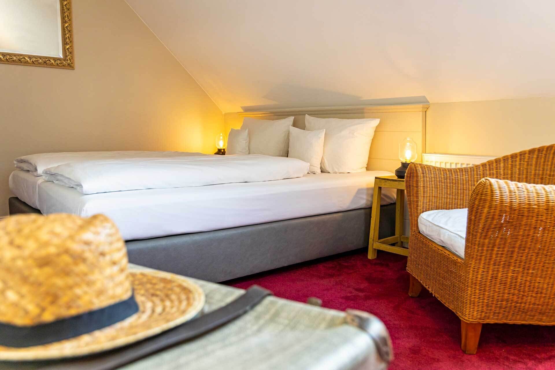 A bedroom with a bed, a nightstand, a wicker chair, and a red carpet.
