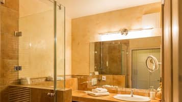 A modern bathroom with a glass shower enclosure, a large mirror, and a beige tiled wall.