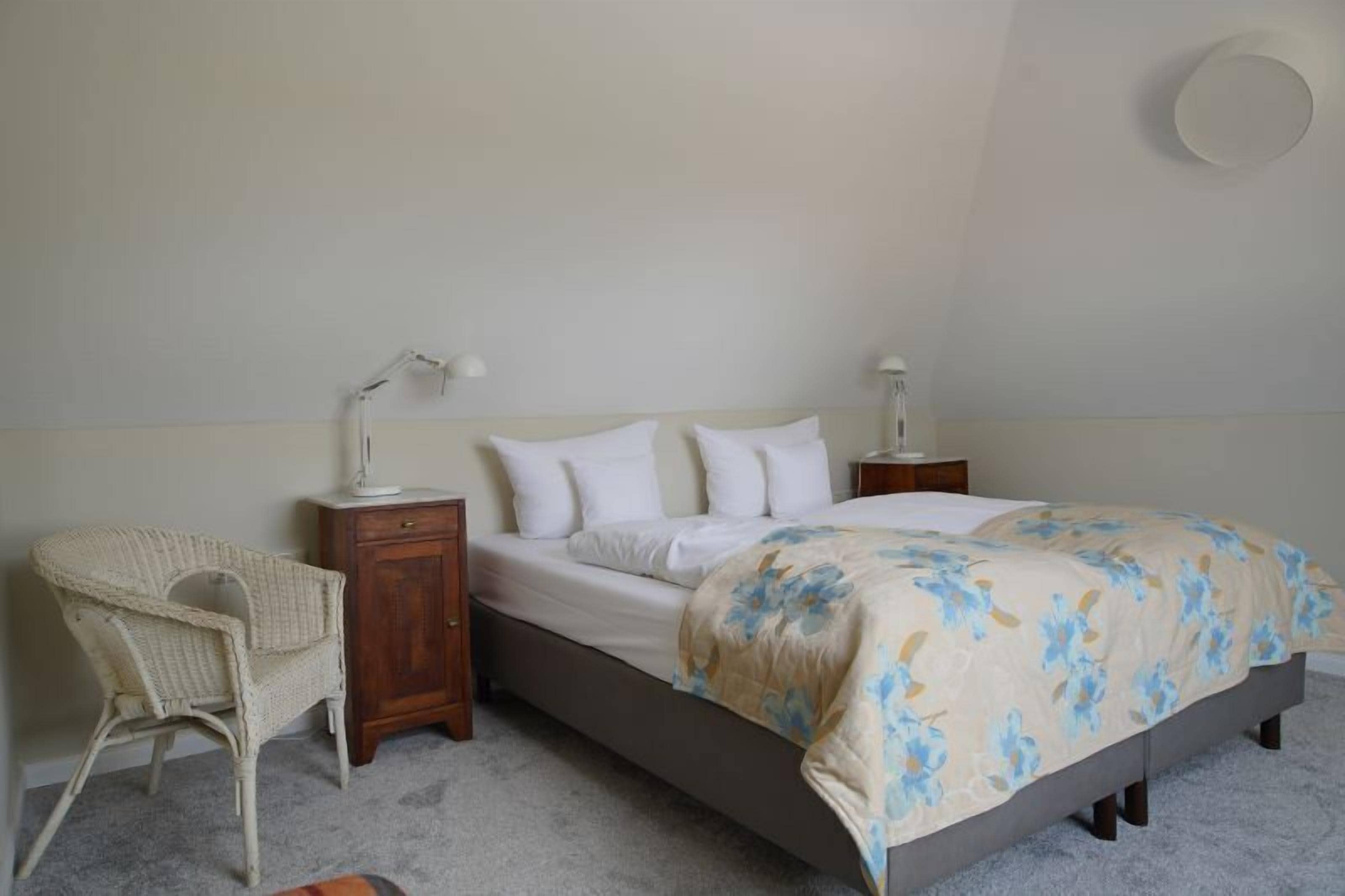 Une chambre à coucher comprenant un lit, deux tables de chevet, une petite table, une chaise et un luminaire fixé au mur.