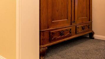A wooden wardrobe with two doors and a small drawer, located in a room with beige walls and a carpeted floor.