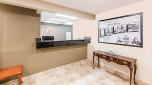 Een receptiezone met een balie, een bord met welkomstboodschap, een houten bank en een console tafel met een decoratief object.
