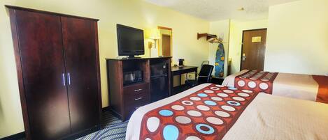 Une chambre d’hôtel avec deux lits, une télévision, un bureau avec un ordinateur, une armoire et un espace douche.