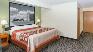 Een hotelkamer met een bed, twee bedlampen, een groot gepresenteerd schilderij aan de muur en een kamerbreed tapijt met dessin.