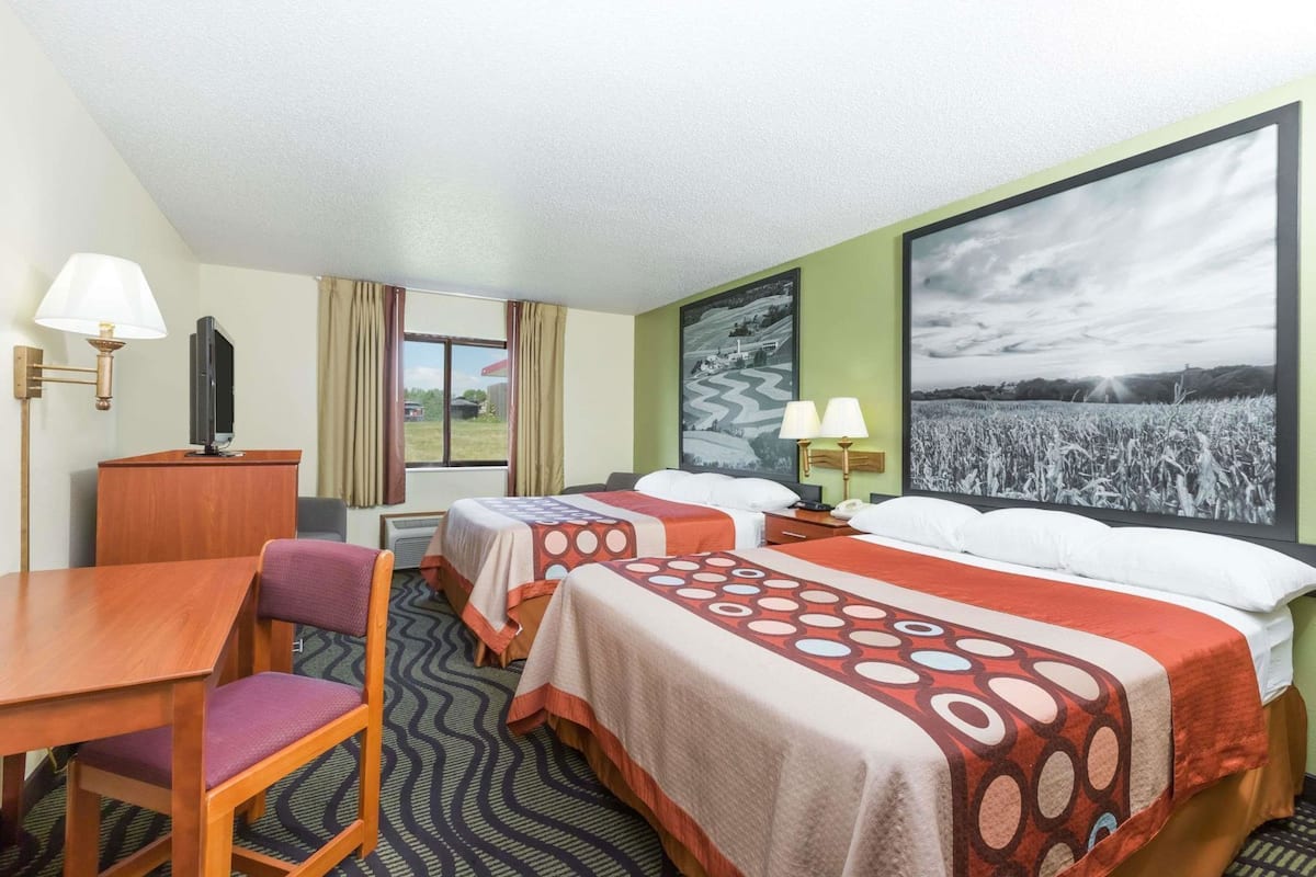 Een hotelkamer met twee bedden, een bureau, een stoel, een televisie en een groot raam.