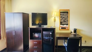 Een hotelkamer met een inloopkast, een televisie, een bureau met lamp, een koffiezetapparaat en een lijst aan de muur.