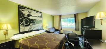 Una habitación de hotel con una cama grande, dos lámparas de noche, un escritorio con televisor y un amplio ventanal con cortinas.