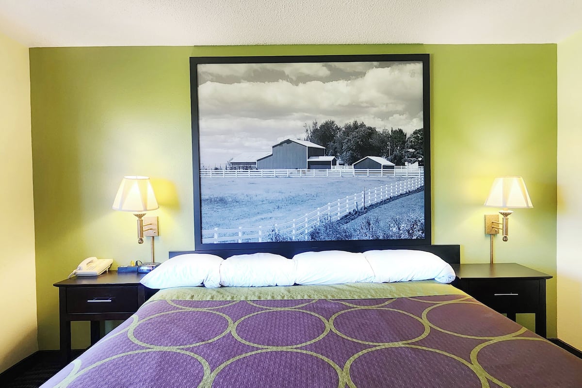 Een hotelkamer met een groot bed, twee nachtkastjes met lampen, een ingelijst kunstwerk aan de muur, en een telefoon op één van de nachtkastjes.