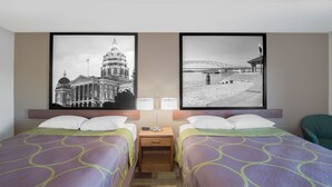 A hotel room with two beds, a nightstand, two wall-mounted lamps, and two framed pictures on the wall.