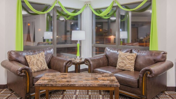 A room with two brown leather sofas, a small wooden table, and green drapes over windows.