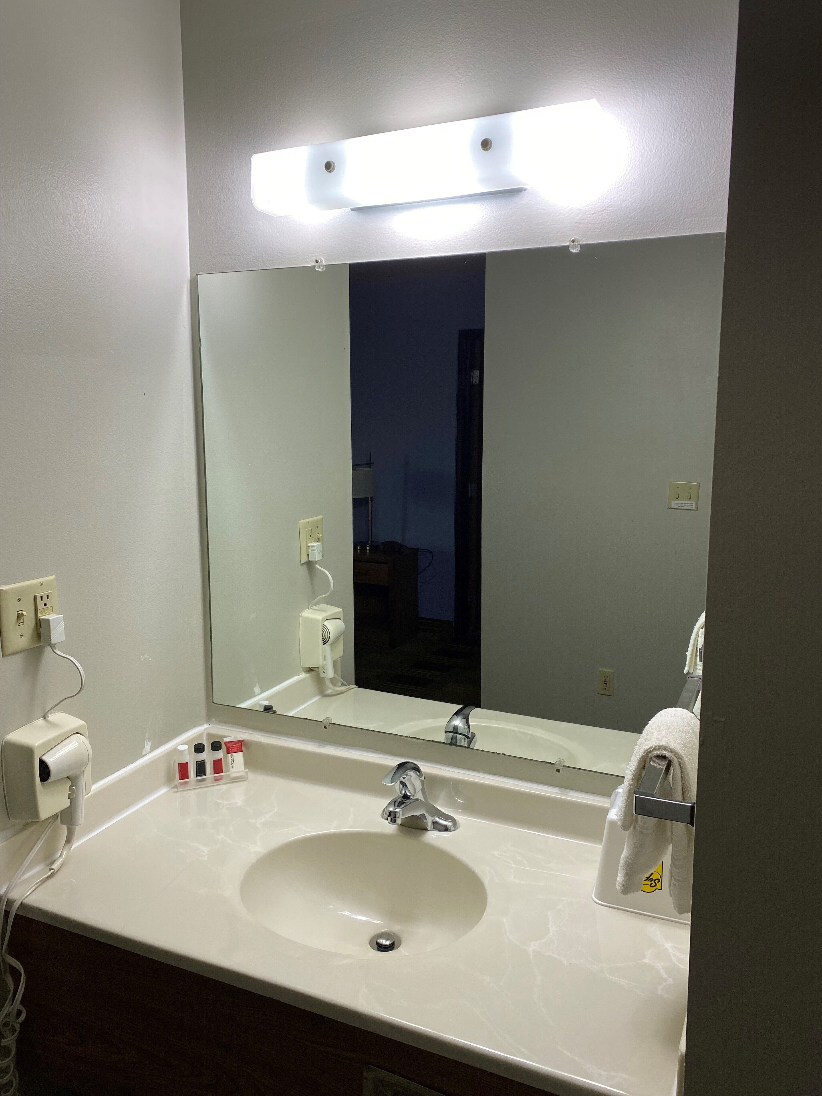 Un baño de hotel con un lavabo blanco, un espejo y una lámpara sobre el espejo.