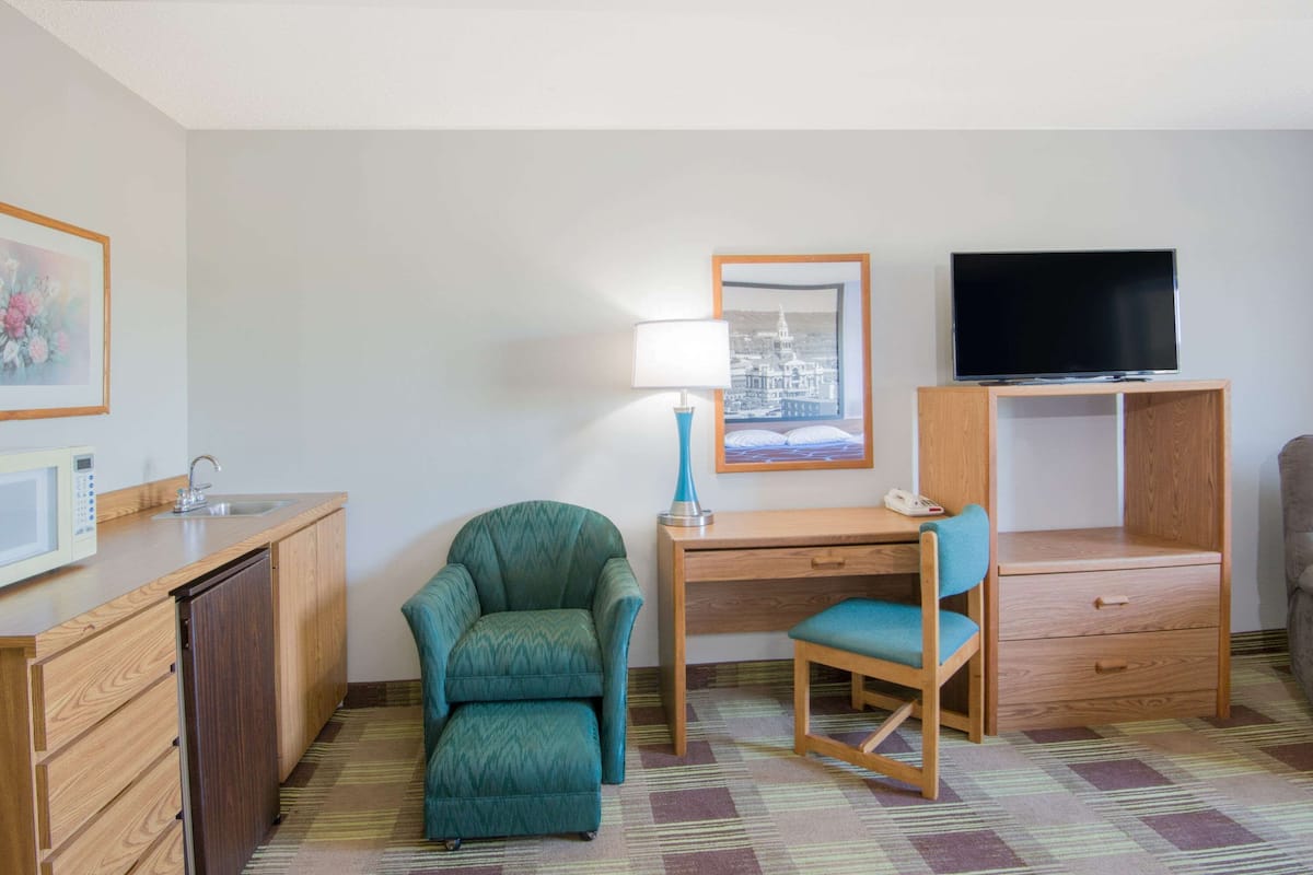 Quarto de hotel com cozinha compacta, escrivaninha com cadeira, televisão e cama.