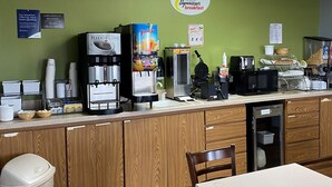 A breakfast area with a coffee machine, juice dispenser, toaster, and a sign for complimentary breakfast.