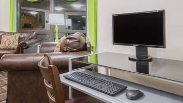 Une chambre d’hôtel avec un canapé en cuir, un bureau en verre doté d’un clavier et d’une souris, et un écran Samsung.