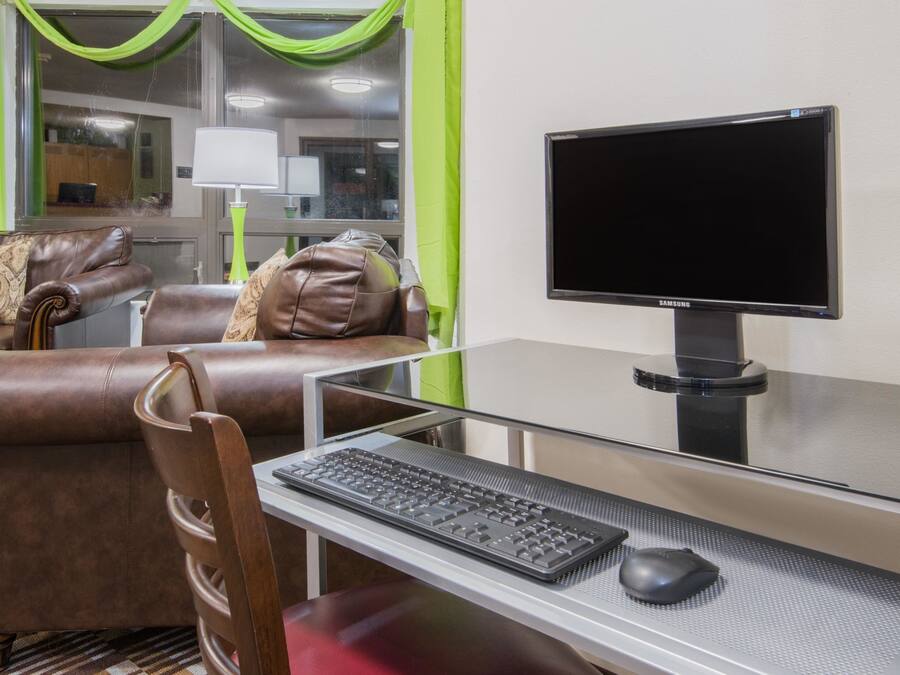 Habitación de hotel con sofá de cuero, un escritorio de vidrio con teclado y ratón, y un monitor Samsung.