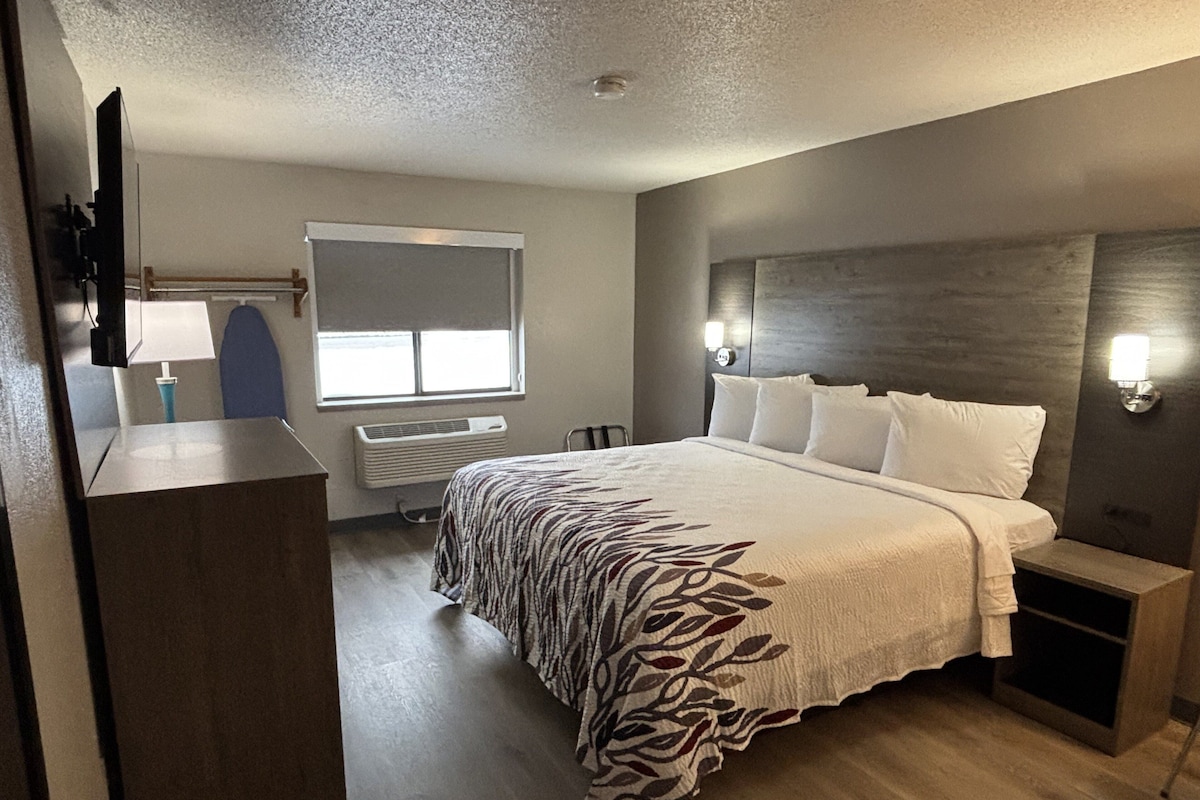 Ein modernes Hotelzimmer mit einem großen Bett, einem Schreibtisch, einem Stuhl, einem Fenster und einem an der Wand befestigten Fernseher.