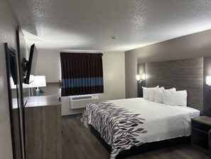 Une chambre d’hôtel dotée d’un grand lit, d’un téléviseur à écran plat, d’une table de chevet, d’une lampe, d’une fenêtre avec des rideaux et d’un luminaire fixé au mur.