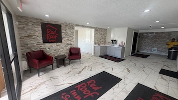 Vestíbulo de Red Roof Inn con pared de piedra, dos sillones rojos, una mesita, una zona de cocina y una persona con una camiseta amarilla.