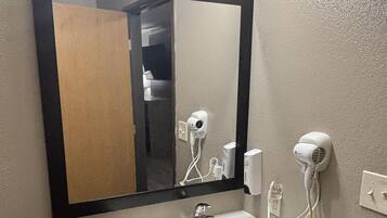 Une salle de bain avec un lavabo blanc, un miroir avec éclairage intégré et deux sèche-cheveux fixés au mur.