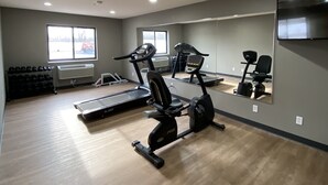 Un gimnasio con equipo cardiovascular, un espejo grande y una televisión.