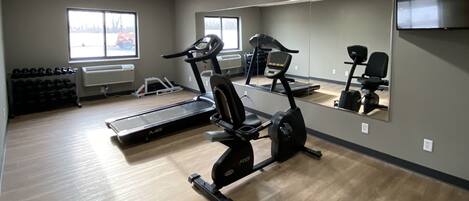 A gym with cardio equipment, a mirrored wall, and a TV.