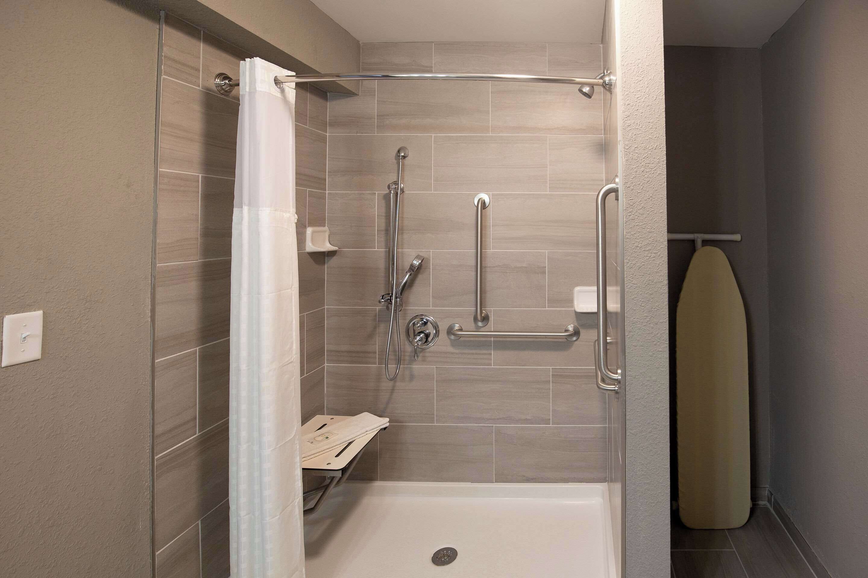 Ducha con puerta de vidrio, cabezal de ducha manual, grifo de mano y barra de apoyo.