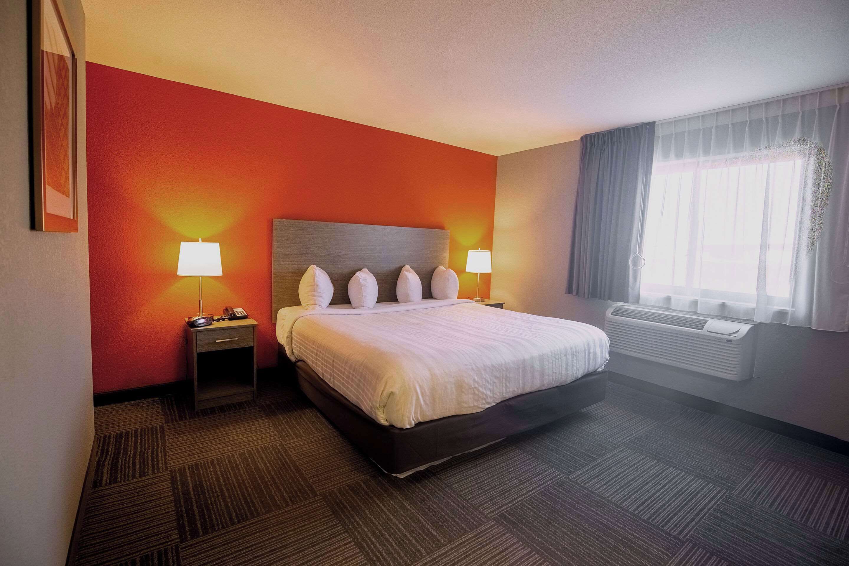 Habitación de hotel con cama, lámparas de noche, un calentador y una ventana con cortinas.